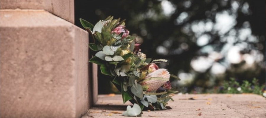 En krans sett fra siden med grønne blader og rosa blomster er plassert foran en gravstøtte. Foto.